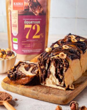 Babka, brioche au chocolat sur une planche en bois à côté d'un sachet de chocolat de la marque Kaoka