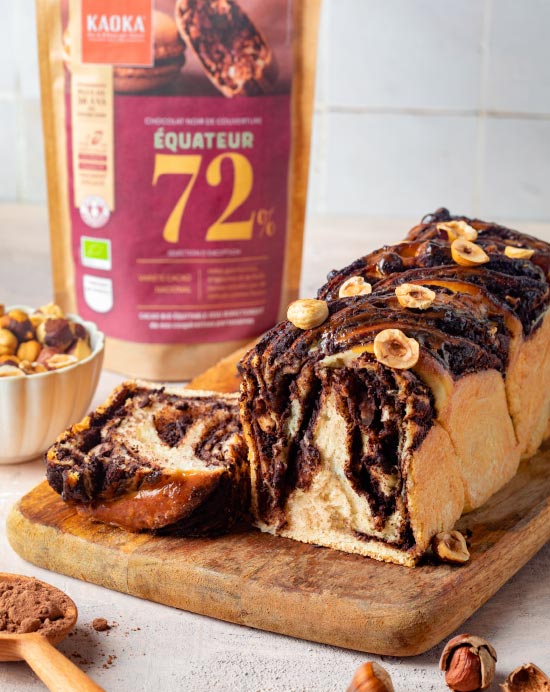 Babka, brioche au chocolat sur une planche en bois à côté d'un sachet de chocolat de la marque Kaoka