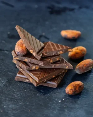 Pile de carrés de chocolat aux éclats de fèves de cacao caramélisés avec des fèves de cacao sur une ardoise