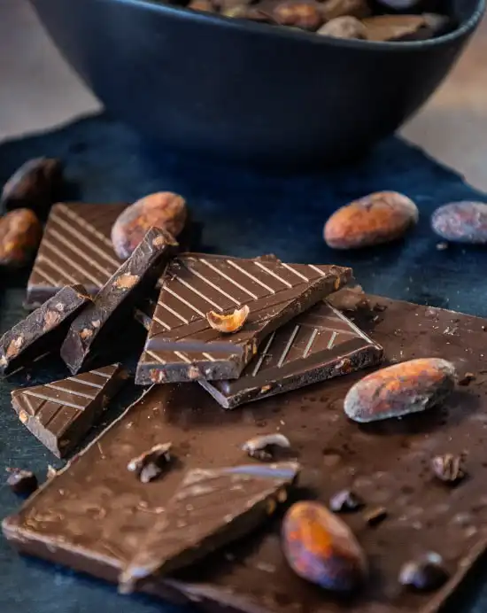 Pile de carrés de chocolat aux éclats de fèves de cacao caramélisés avec des fèves de cacao sur une ardoise