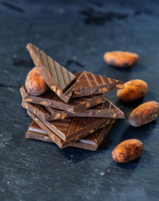 Pile de carrés de chocolat aux éclats de fèves de cacao caramélisés avec des fèves de cacao sur une ardoise