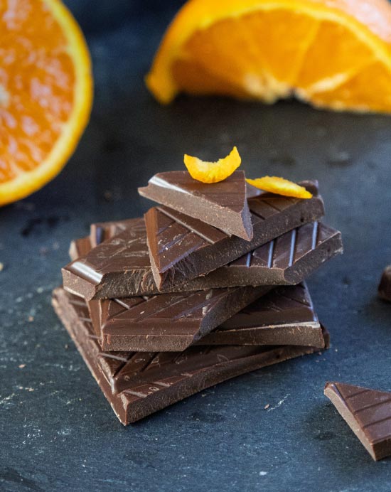 Pile de carreaux de chocolat noir à l'huile essentielle d'orange avec des tranches d'orange sur une ardoise