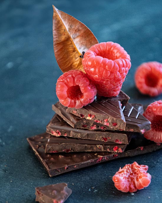 Pile de carrés de chocolait noir aux pépites de framboises avec des framboises fraîches