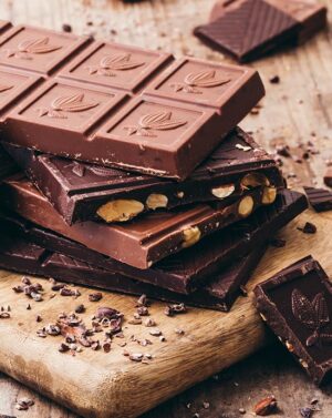 Plusieurs tablettes de chocolat noir et lait empilées sur une planche en bois, chocolat bio et équitable de la marque Kaoka